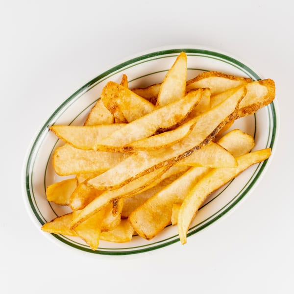 Golden-brown thick-cut French fries piled on a white plate with green trim.