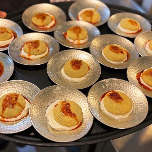 Numerous plated golden pastries with creamy filling and caramelized topping arranged on hammered silver plates.