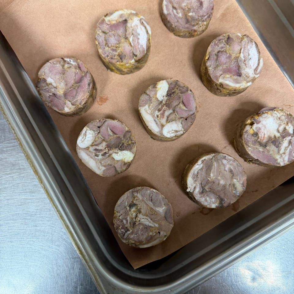Sliced meat roulades with marbled layers arranged on parchment in a metal baking tray.