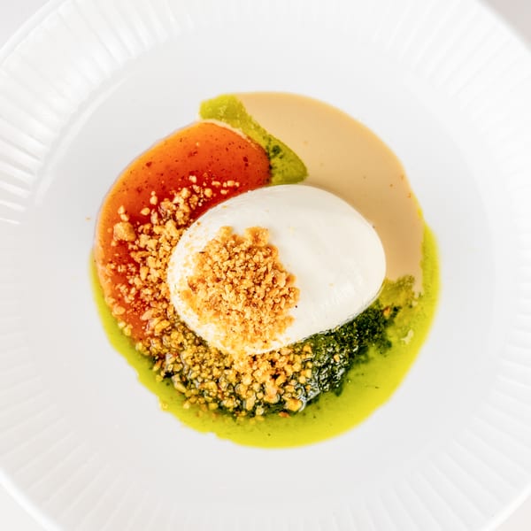 Burrata topped with crunchy crumbs, surrounded by red, green, and creamy sauces on a white plate.