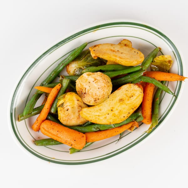 Roasted carrots, green beans, and sliced root vegetables arranged on a green-rimmed serving platter.