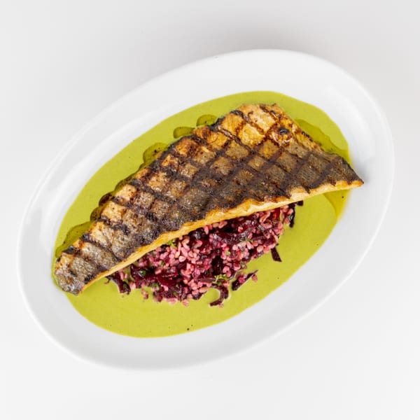 Grilled fish fillet served over beetroot rice with creamy green herb sauce on a white plate.