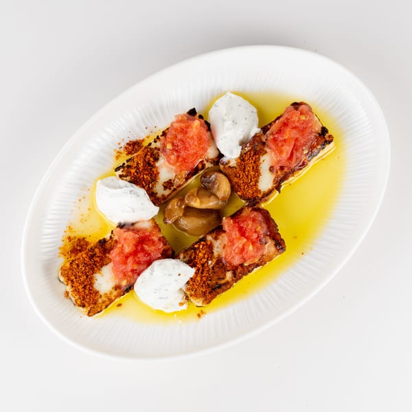 Grilled chicken pieces topped with chopped tomatoes, creamy herb sauce, and crispy crumbs, served with roasted garlic in olive oil.