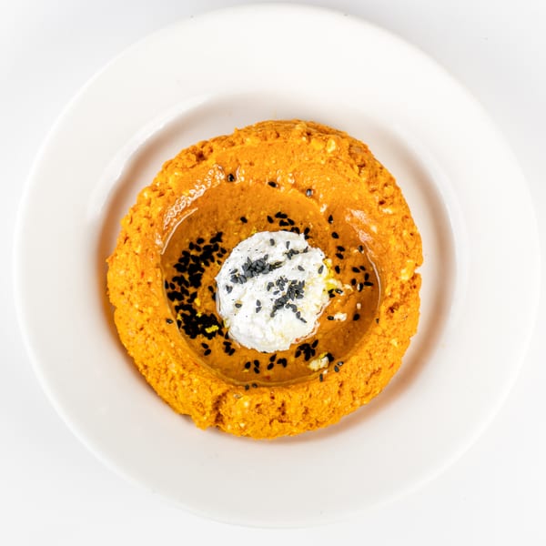 Orange ring-shaped pastry filled with creamy white topping and black sesame seeds on a white plate.