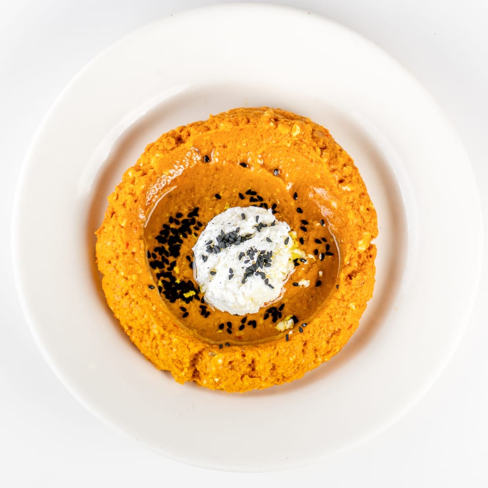 Orange ring-shaped pastry filled with creamy white topping and black sesame seeds on a white plate.