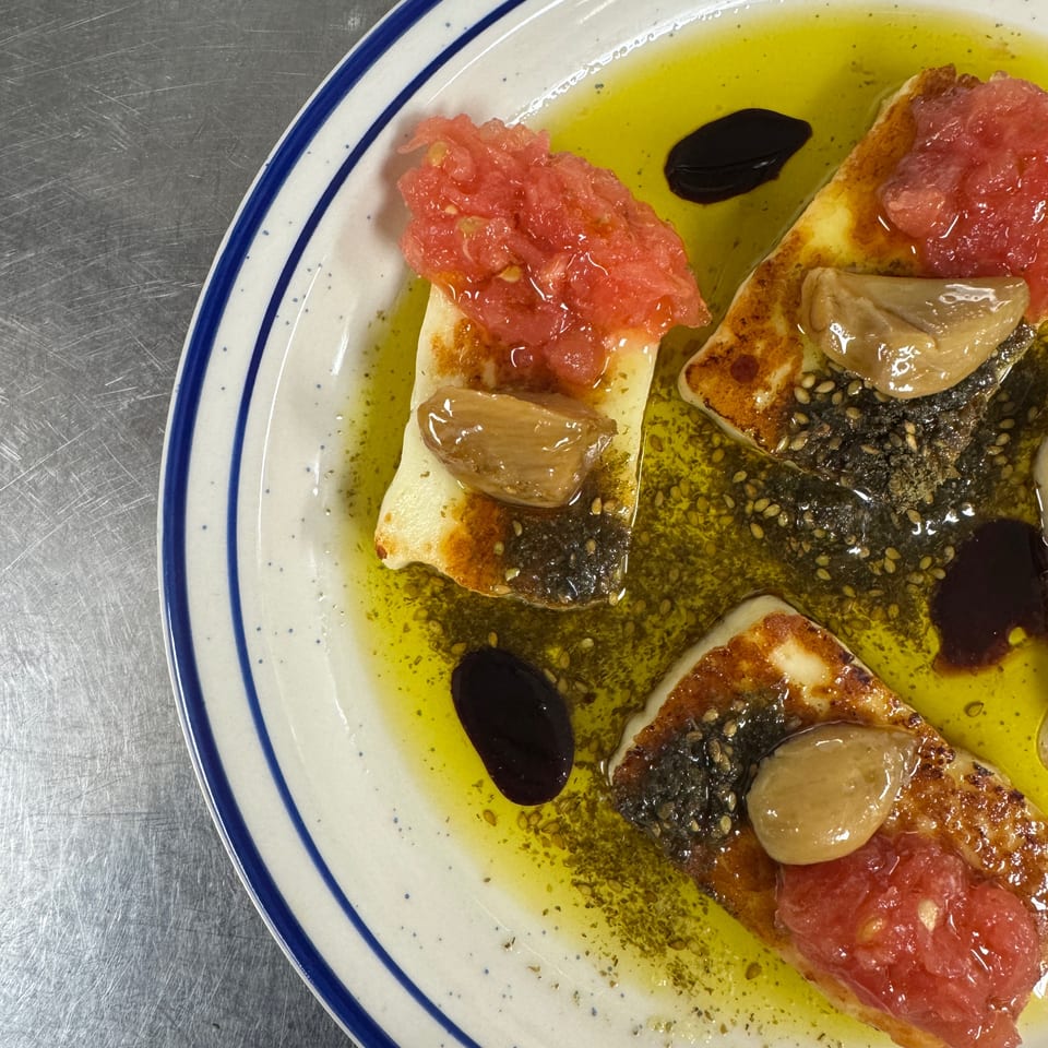 Toasted bread topped with crushed tomatoes, roasted garlic, black olives, and herbs in olive oil on a blue-rimmed plate.