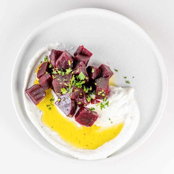 Roasted beet cubes with fresh herbs, olive oil, and creamy white sauce on a white plate.
