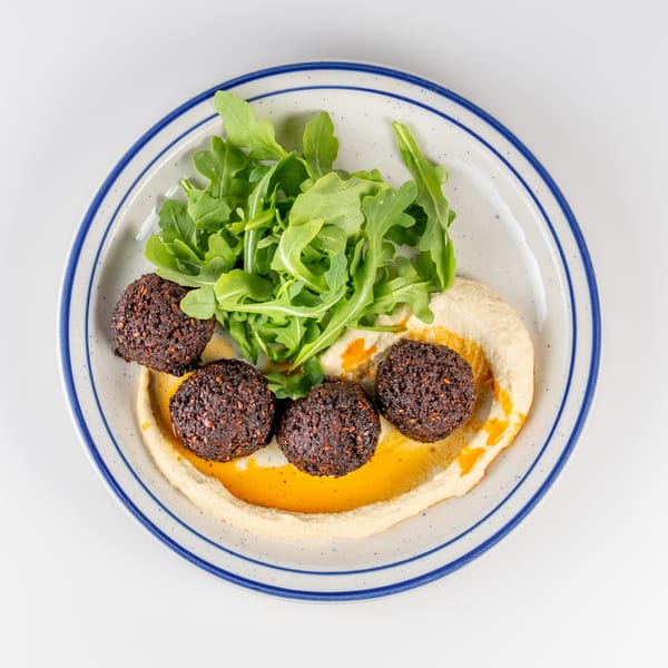 Overhead view of falafel, hummus, arugula, and chili oil on a blue-rimmed plate.