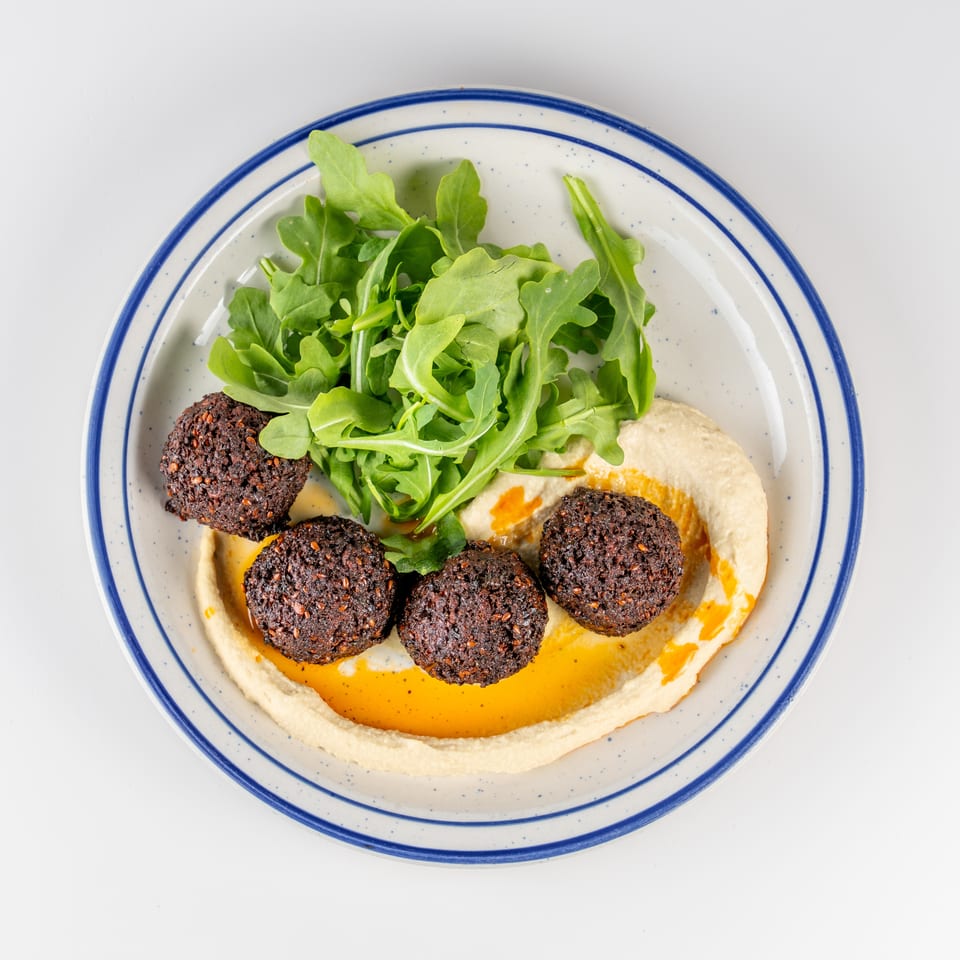 Overhead view of falafel, hummus, arugula, and chili oil on a blue-rimmed plate.