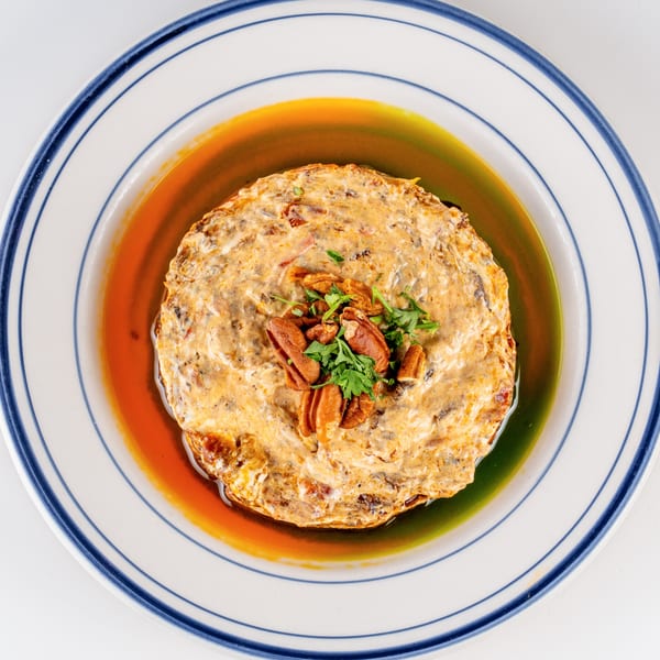 Creamy savory casserole topped with pecans and parsley, surrounded by colorful sauce on a blue-rimmed plate.