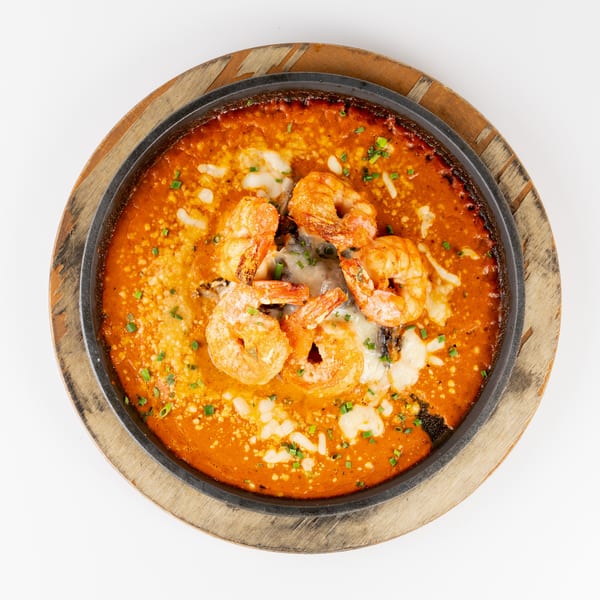 Overhead view of a sizzling skillet filled with shrimp, melted cheese, and orange sauce, garnished with chopped green onions.