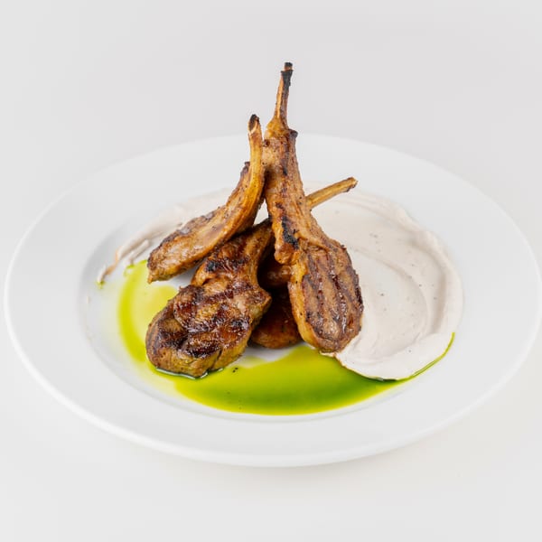 Grilled lamb chops arranged on creamy sauce with bright green herb oil on a white plate.