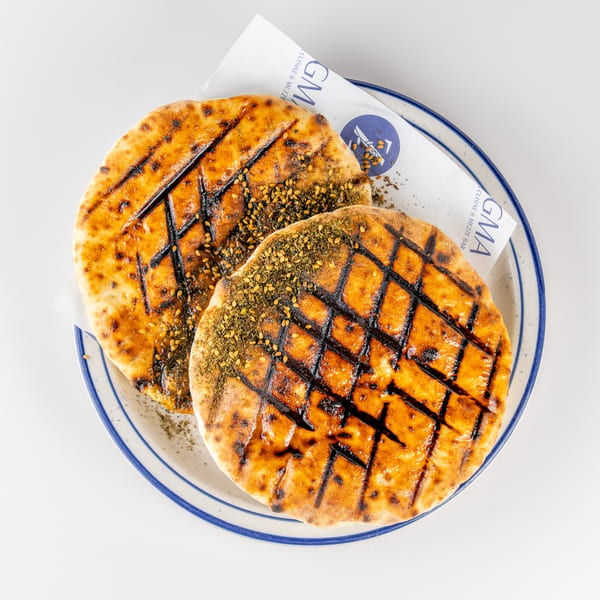 Two grilled flatbreads topped with za’atar and sesame seeds, served on a blue-rimmed plate.