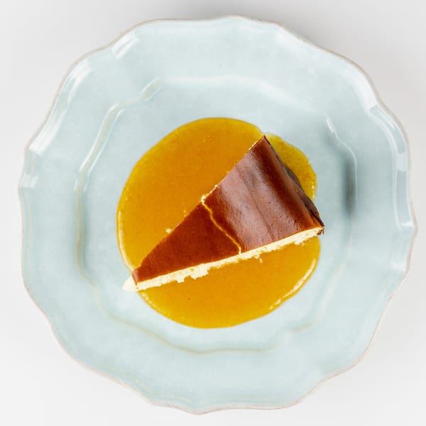 Slice of chocolate cake with cream filling on golden sauce, served on a pale blue scalloped plate.