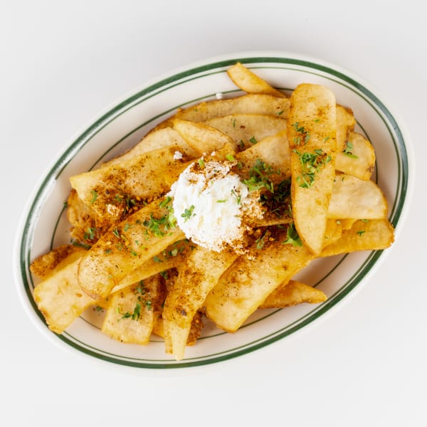 Seasoned golden fries topped with crumbled white cheese and fresh herbs in a green-rimmed dish.