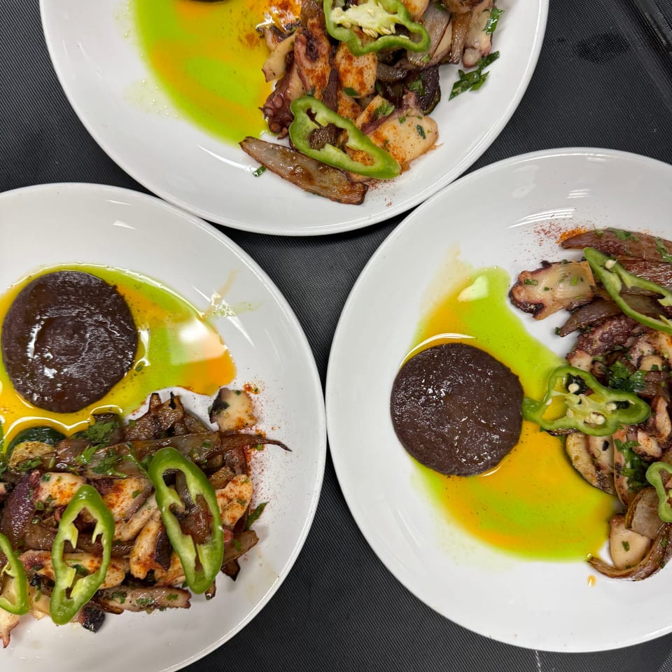 Three plates of grilled octopus and seafood with green peppers, herbs, olive oil, and dark dipping sauce.