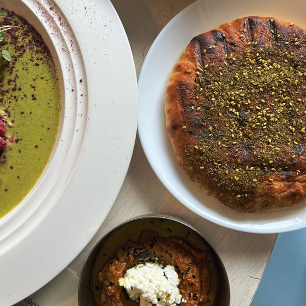Overhead view of Middle Eastern dishes, including za’atar flatbread, green dip, and roasted red pepper spread topped with feta.