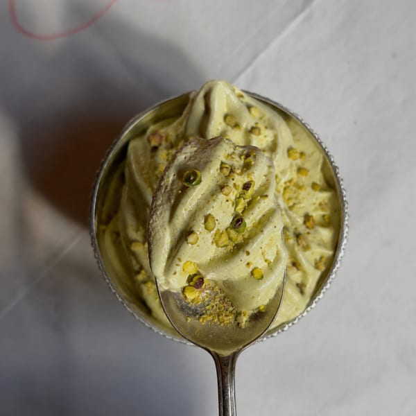 Pistachio ice cream topped with crushed pistachios, served in a glass bowl with a spoon.