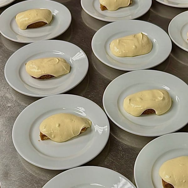 Multiple plated pastries topped with thick pale frosting arranged across a commercial kitchen work surface.