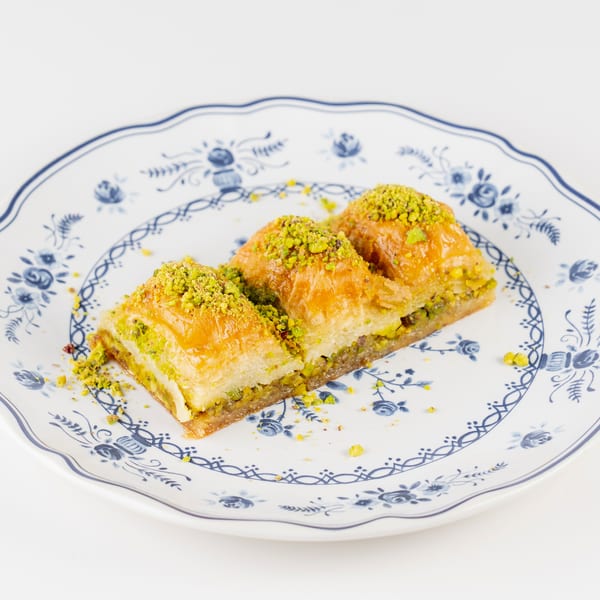 Pistachio-topped baklava pastries arranged on a blue-and-white floral plate.