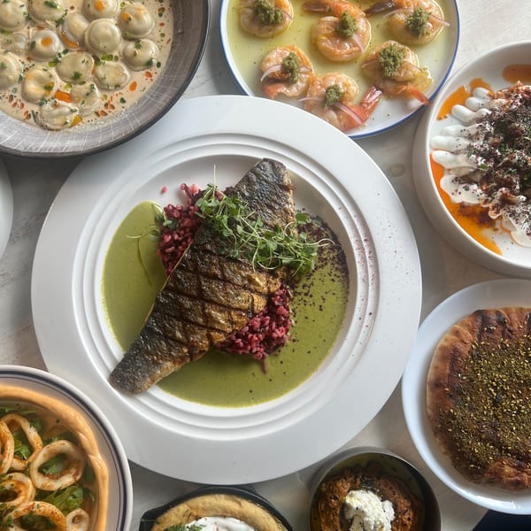 Overhead spread of Mediterranean dishes featuring grilled fish, shrimp, creamy dumplings, calamari, dips, and za’atar flatbread.