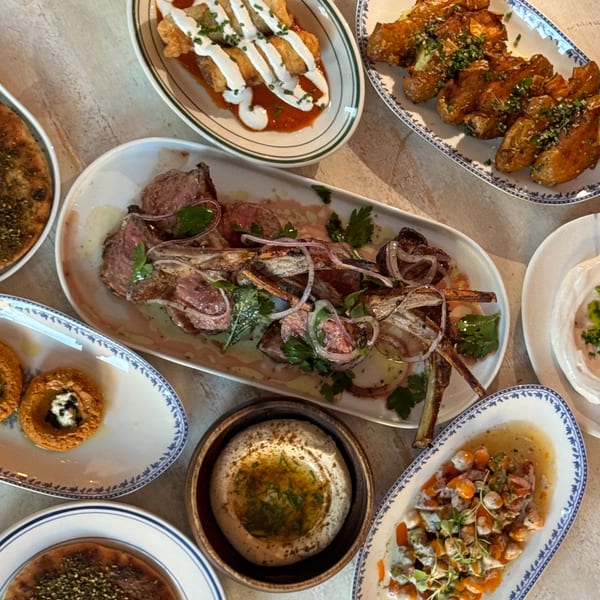 Overhead spread of Middle Eastern dishes, including fried appetizers, roasted meat, hummus, and colorful salads on patterned plates.