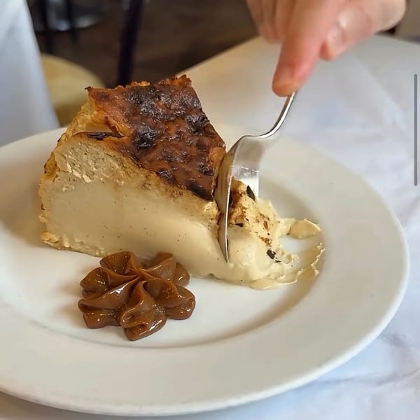 Slice of creamy layered dessert topped with caramelized pastry, served with glossy caramel garnish as a fork cuts into it.