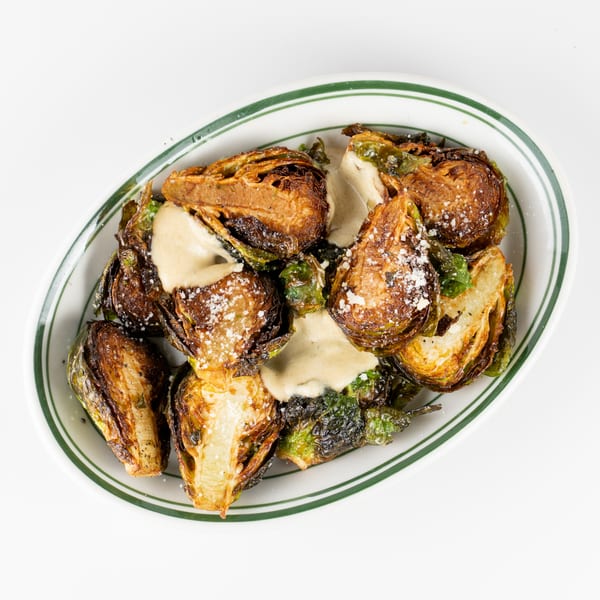 Roasted Brussels sprouts topped with creamy sauce and grated cheese on a white plate.